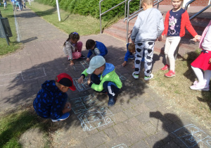 dzieci całą grupa malują kredą wzorki na chodniku